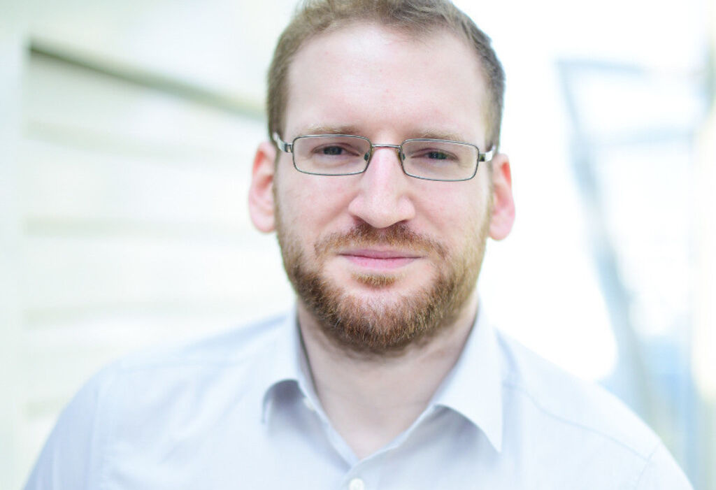 Ein Mann mit kurzen Haaren, Brille und Bart sowie einem hellen Hemd steht in Hamburg. Mit neutralem Gesichtsausdruck blickt er direkt in die Kamera.
