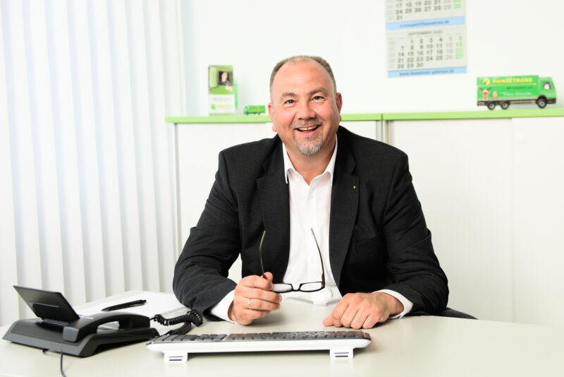 Ein Mann in einem Business-Anzug sitzt an einem Schreibtisch, während sich Essen, Deutschland, auf der Glasscheibe hinter ihm spiegelt.