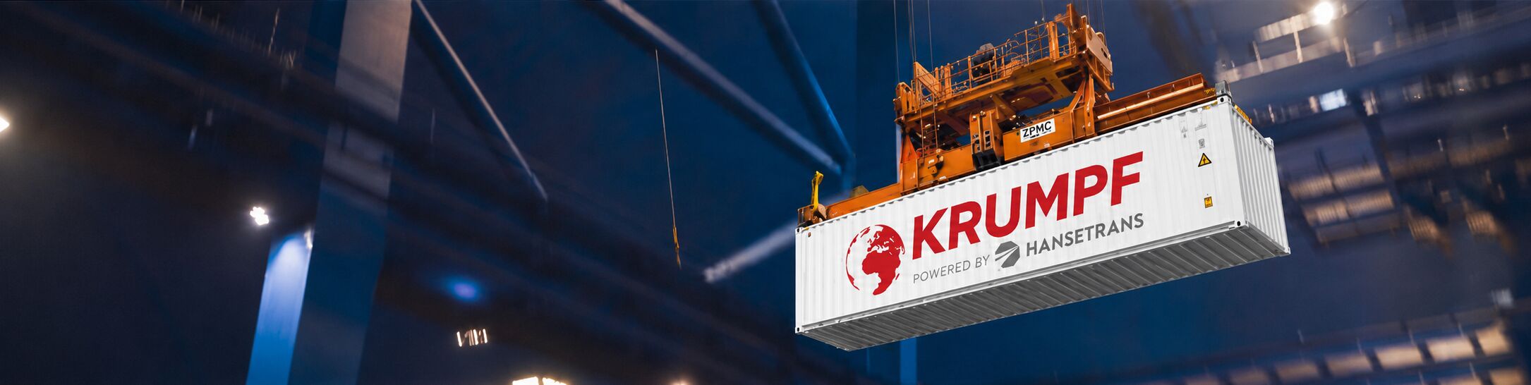 Ein großer Kran hebt in einer Industriehalle einen weißen Frachtcontainer mit der Aufschrift „HANSETRANS“ an.